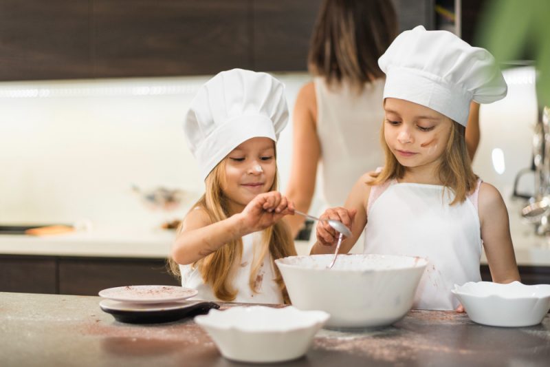 little-siblings-chef-hat-mixing-ingredients-bowl-kitchen-worktop